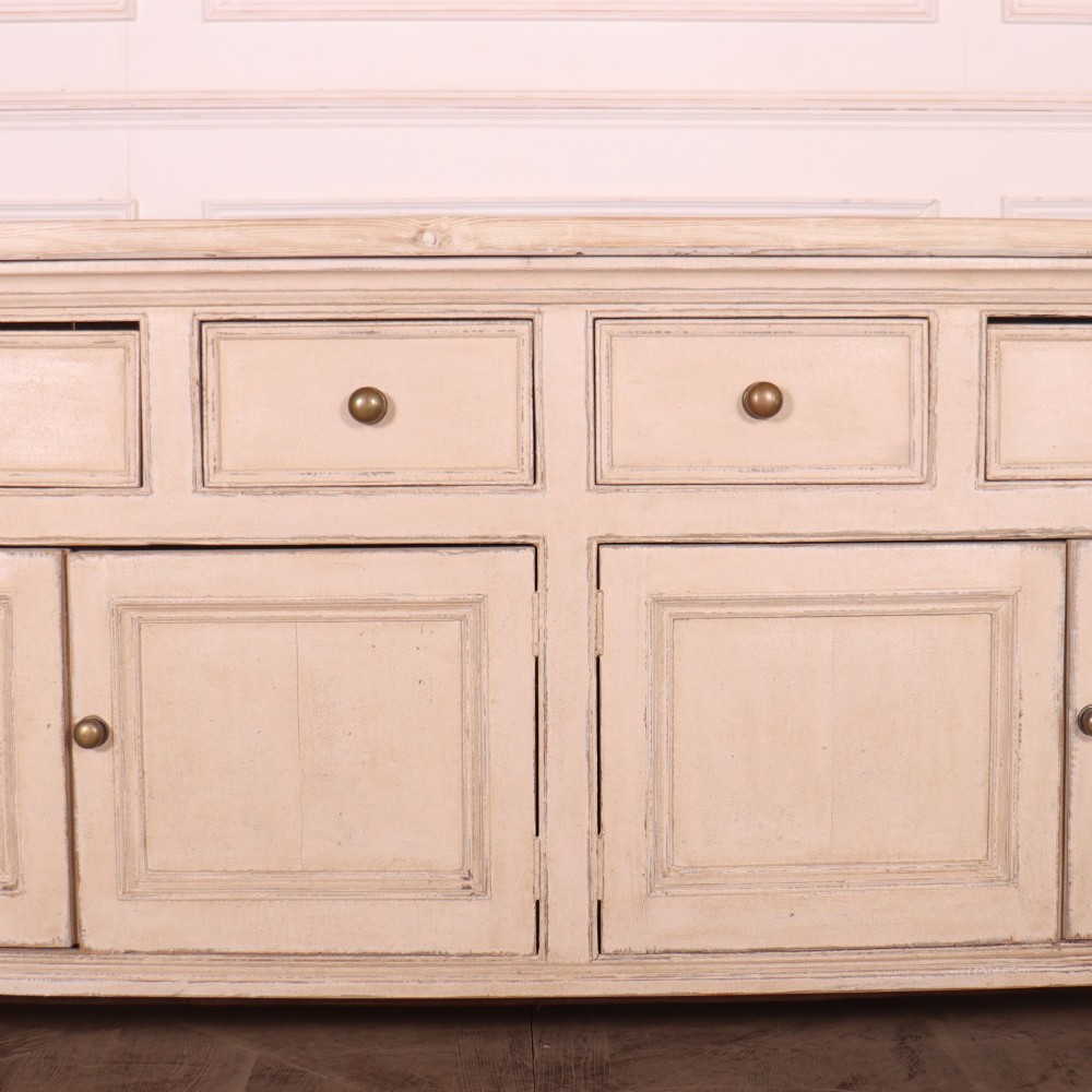 A large off-white painted English dresser base featuring four drawers above four cupboard doors with small brass knob handles. View IV