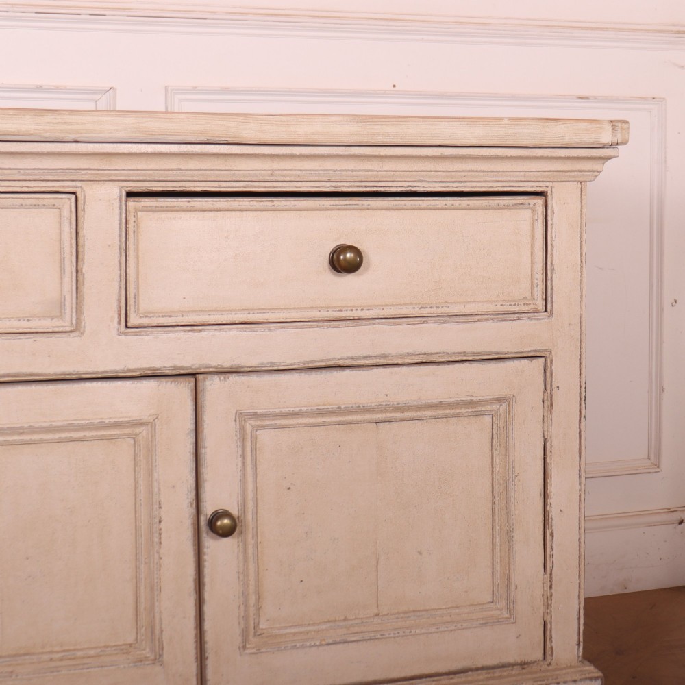 A large off-white painted English dresser base featuring four drawers above four cupboard doors with small brass knob handles. View V