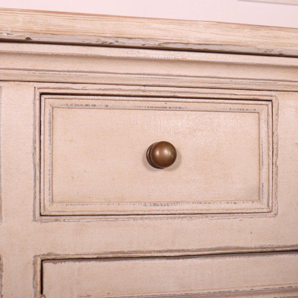 A large off-white painted English dresser base featuring four drawers above four cupboard doors with small brass knob handles. View VII