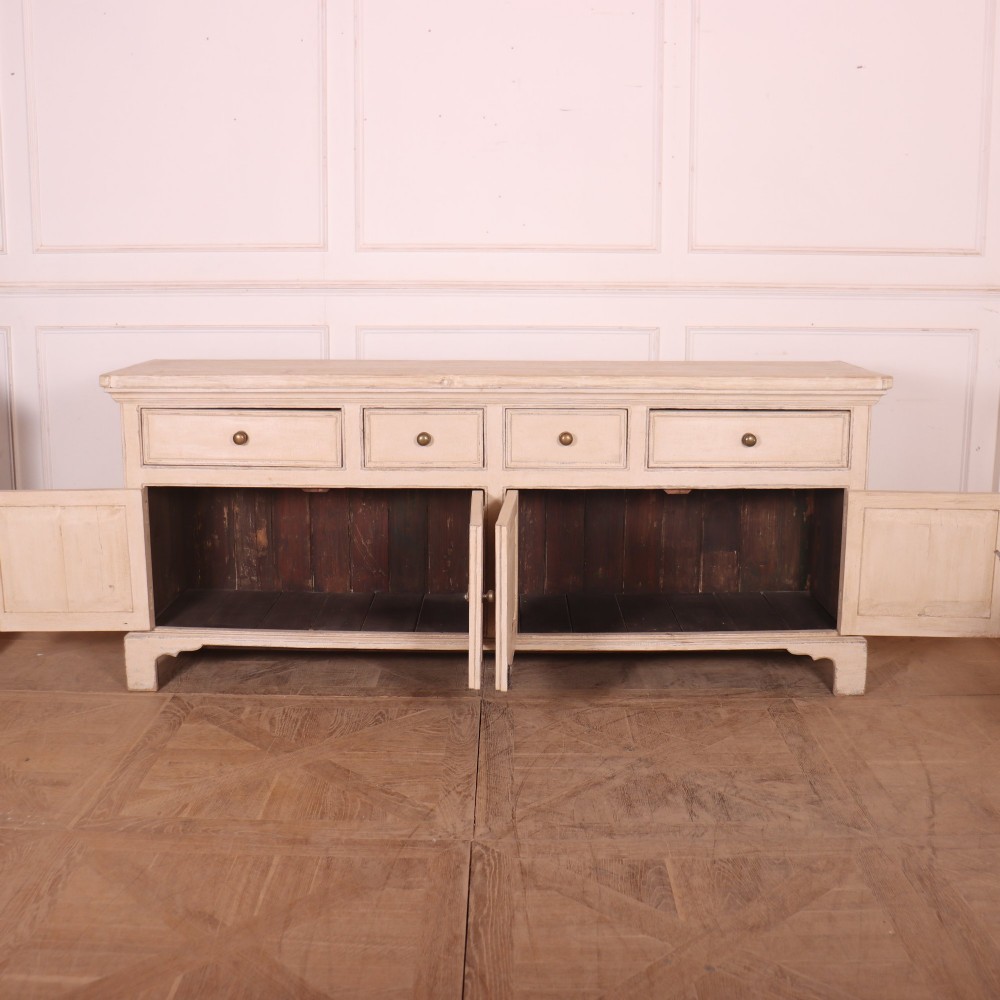 A large off-white painted English dresser base featuring four drawers above four cupboard doors with small brass knob handles. View VIII