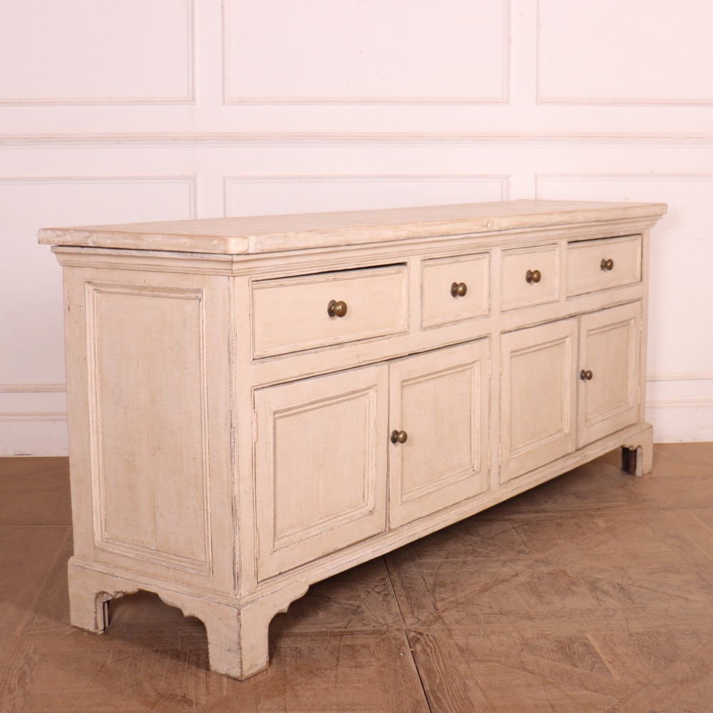 A large off-white painted English dresser base featuring four drawers above four cupboard doors with small brass knob handles. View IX