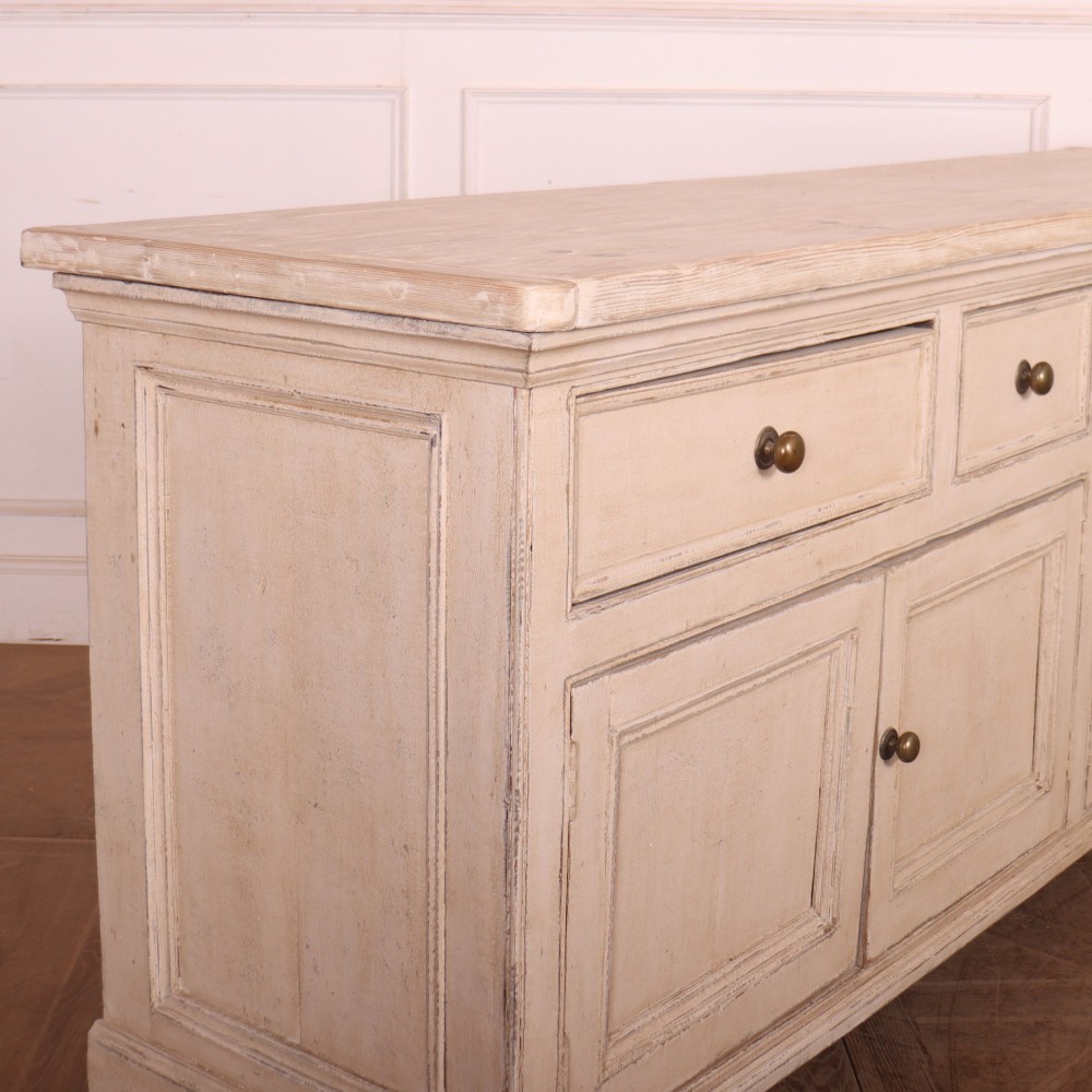 A large off-white painted English dresser base featuring four drawers above four cupboard doors with small brass knob handles. View X