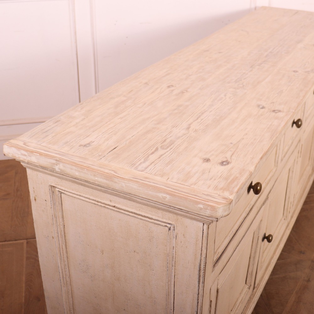 A large off-white painted English dresser base featuring four drawers above four cupboard doors with small brass knob handles. View XII