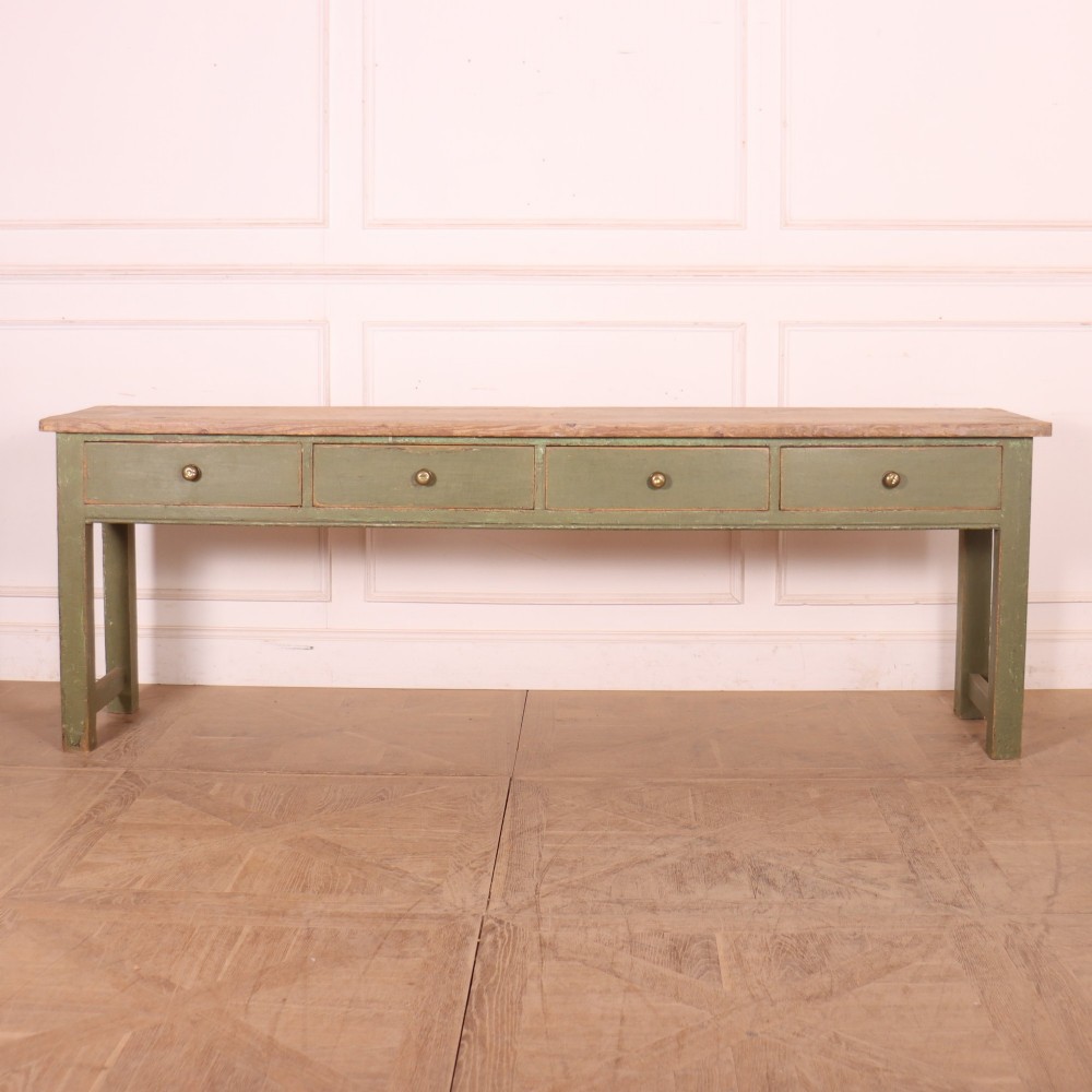 A long antique painted dresser base with four inline drawers, small brass knobs, a green frame, and a scrubbed wooden top.