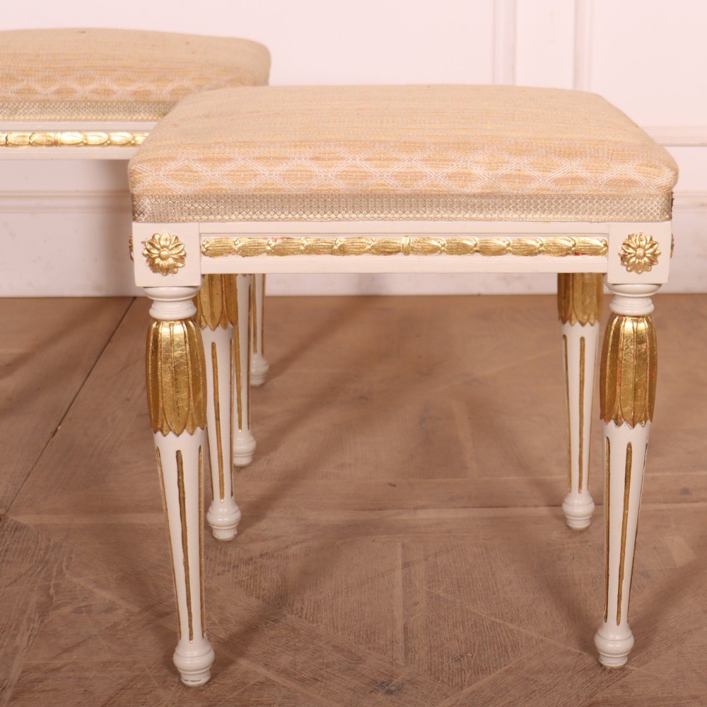 A pair of Neoclassical Swedish Gustavian style footstools with white painted legs, gold leaf fluted details, and cream patterned upholstered seats. View II