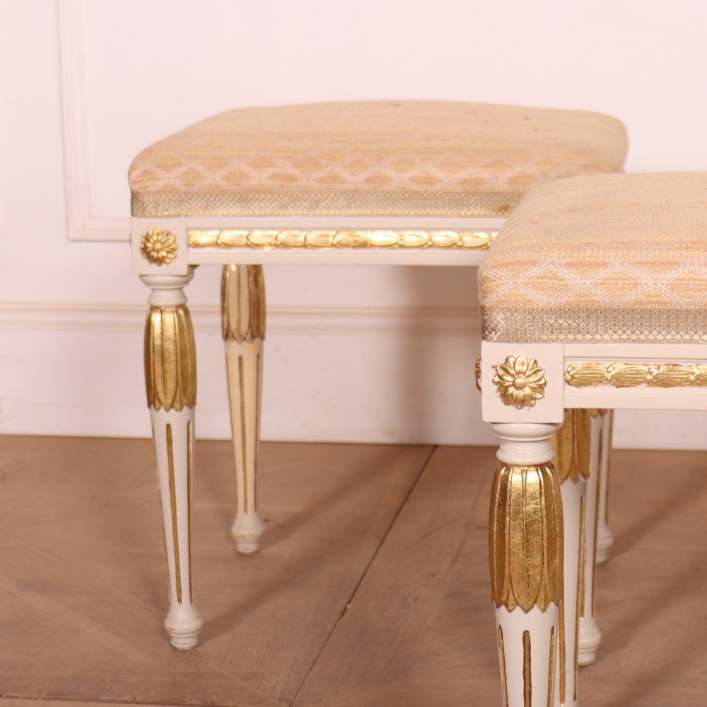 A pair of Neoclassical Swedish Gustavian style footstools with white painted legs, gold leaf fluted details, and cream patterned upholstered seats. View III