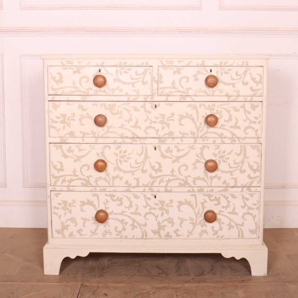 A nineteenth-century cream-painted chest of drawers featuring a beige floral stencil motif across the drawer fronts and turned wooden knobs.