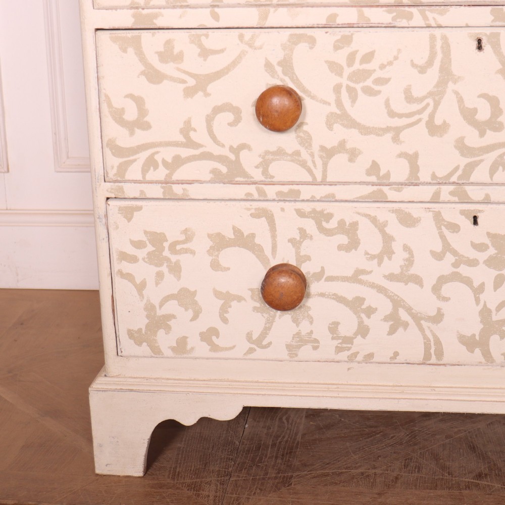 A nineteenth-century cream-painted chest of drawers featuring a beige floral stencil motif across the drawer fronts and turned wooden knobs. View V