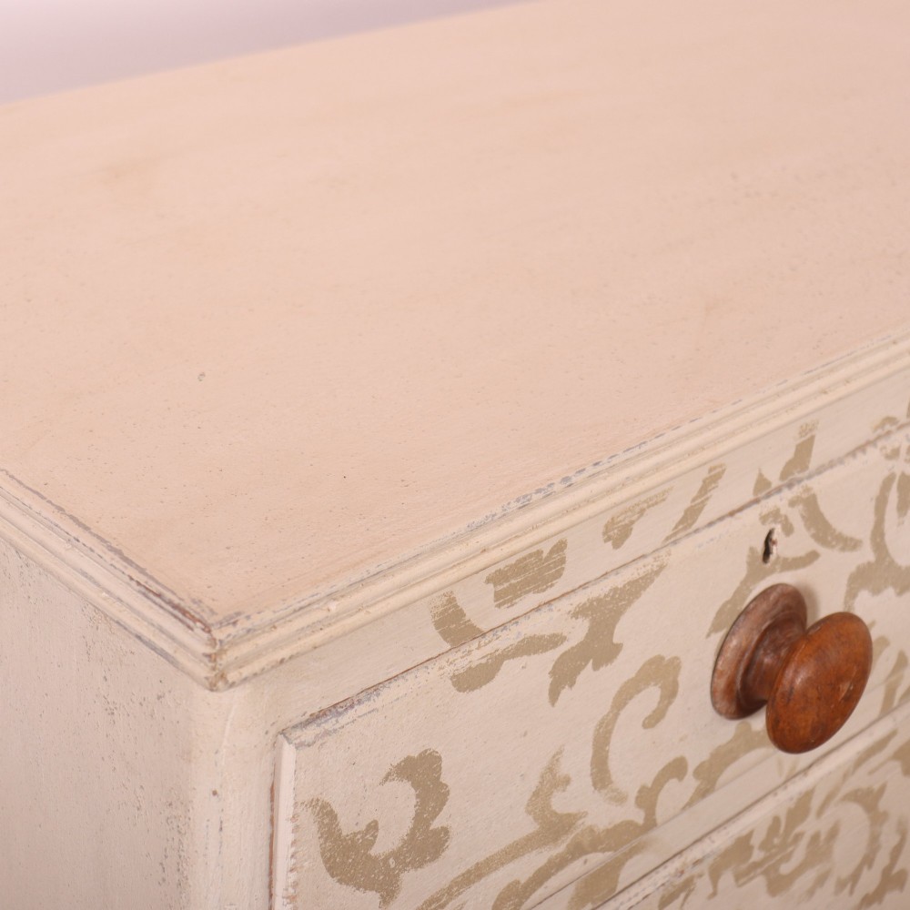 A nineteenth-century cream-painted chest of drawers featuring a beige floral stencil motif across the drawer fronts and turned wooden knobs. View VIII