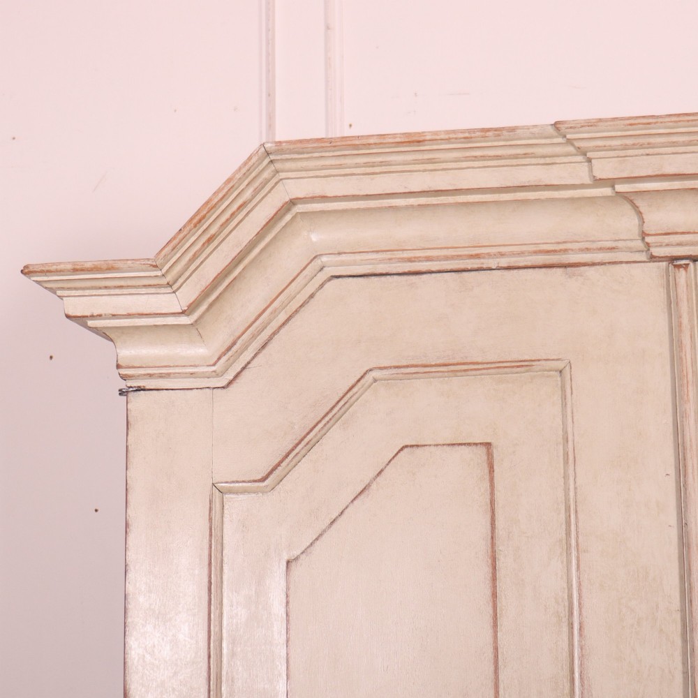 A tall antique Swedish painted linen cupboard featuring shaped panel doors over three drawers with brass handles in an off-white distressed finish. View II