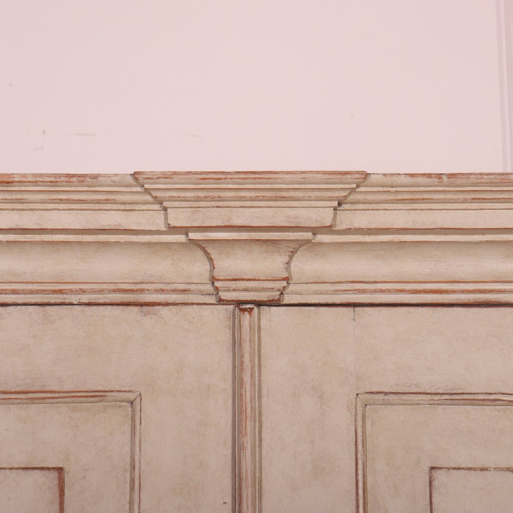 A tall antique Swedish painted linen cupboard featuring shaped panel doors over three drawers with brass handles in an off-white distressed finish. View III