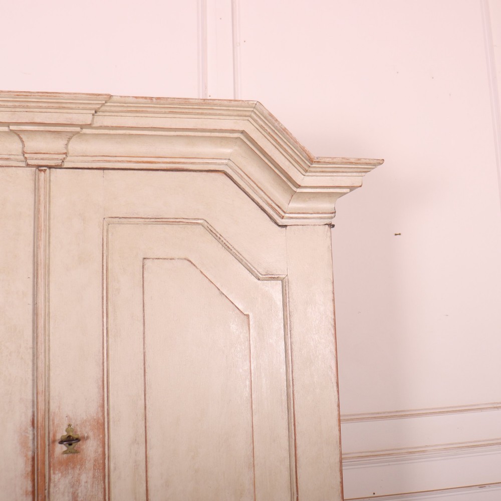 A tall antique Swedish painted linen cupboard featuring shaped panel doors over three drawers with brass handles in an off-white distressed finish. View IV