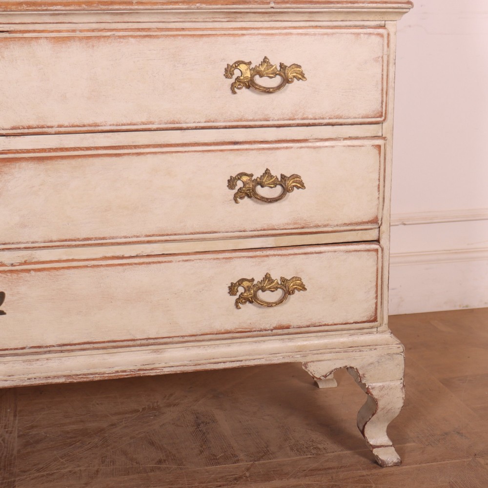 A tall antique Swedish painted linen cupboard featuring shaped panel doors over three drawers with brass handles in an off-white distressed finish. View VI