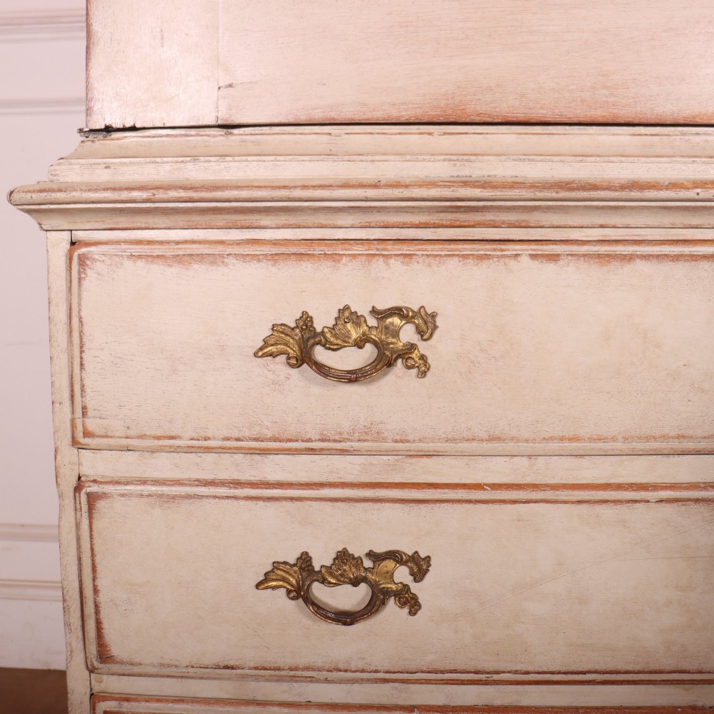 A tall antique Swedish painted linen cupboard featuring shaped panel doors over three drawers with brass handles in an off-white distressed finish. View VII