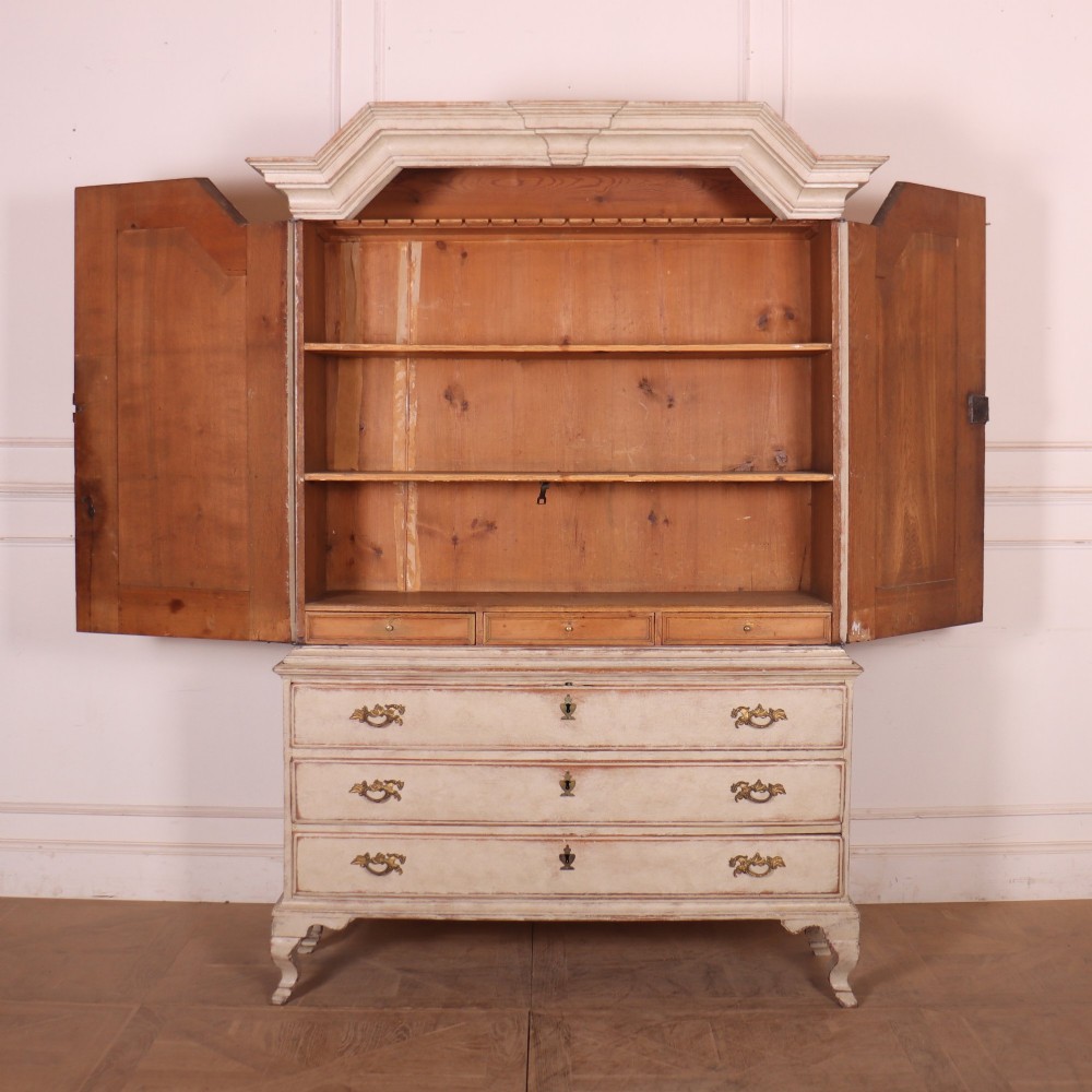 A tall antique Swedish painted linen cupboard featuring shaped panel doors over three drawers with brass handles in an off-white distressed finish. View VIII