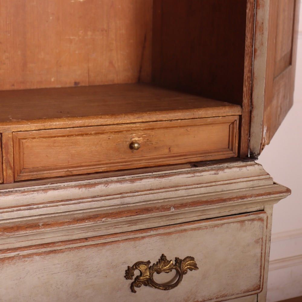 A tall antique Swedish painted linen cupboard featuring shaped panel doors over three drawers with brass handles in an off-white distressed finish. View IX