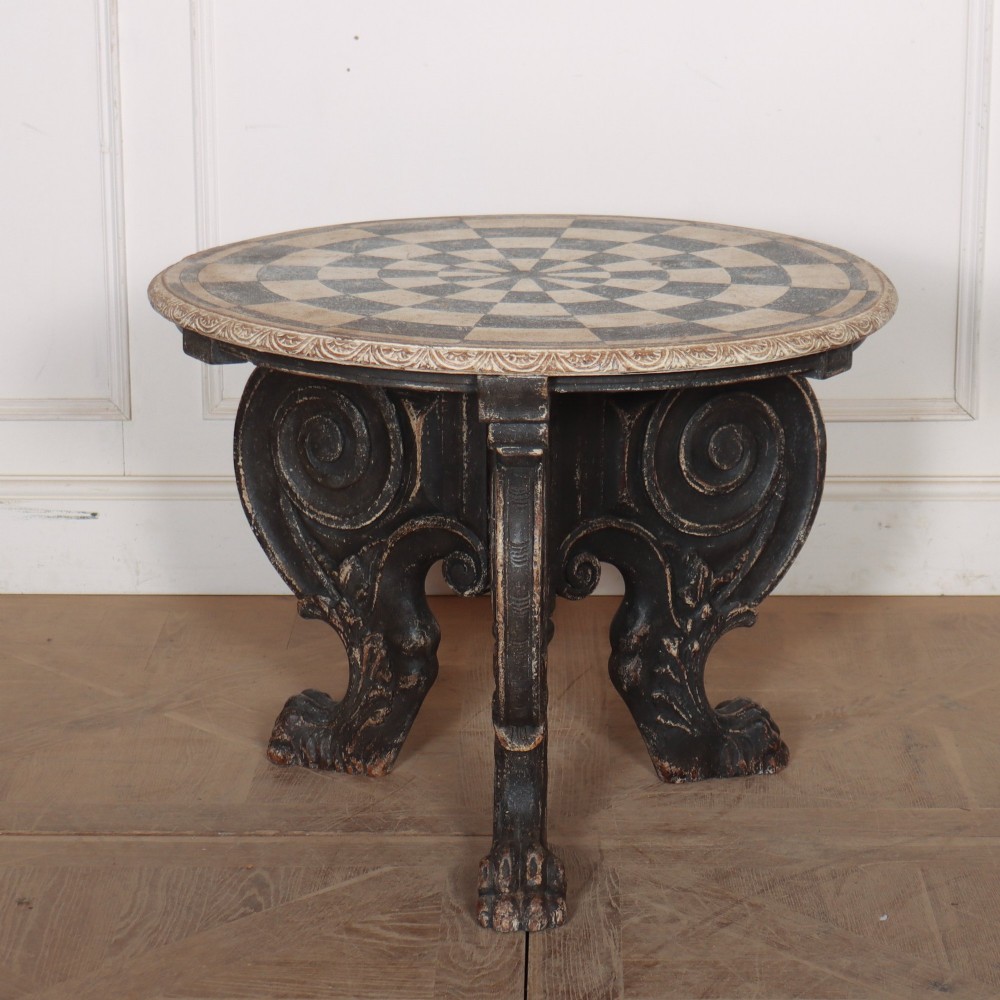 An antique round side table with a cream and grey circular checkerboard top supported by dark carved scroll legs with paw feet.