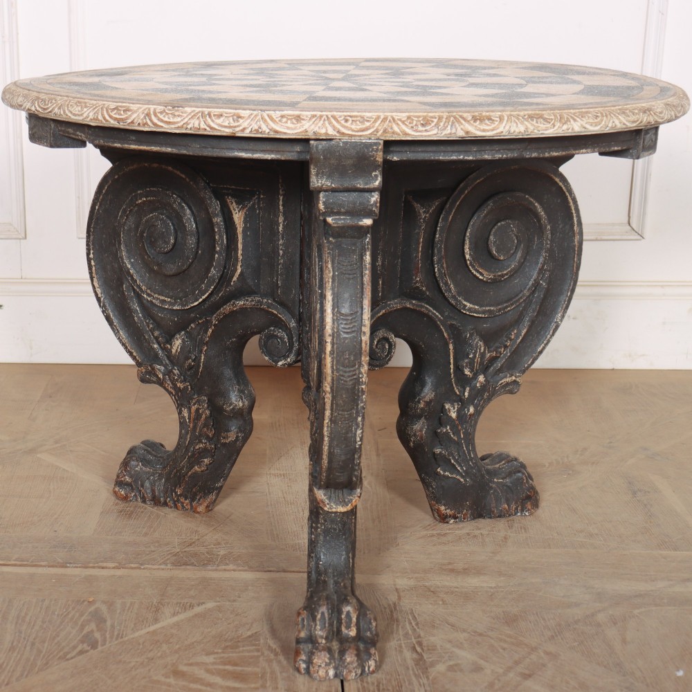 An antique round side table with a cream and grey circular checkerboard top supported by dark carved scroll legs with paw feet. View II
