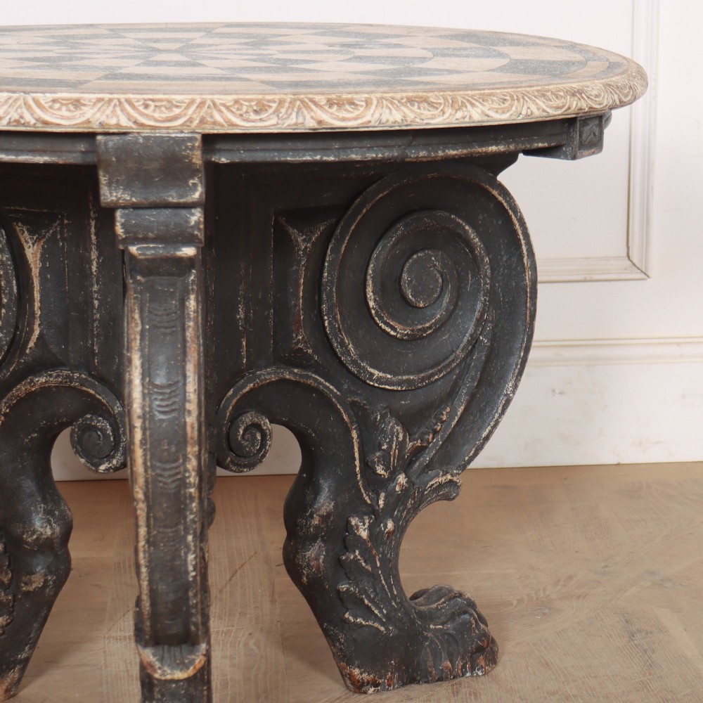An antique round side table with a cream and grey circular checkerboard top supported by dark carved scroll legs with paw feet. View III