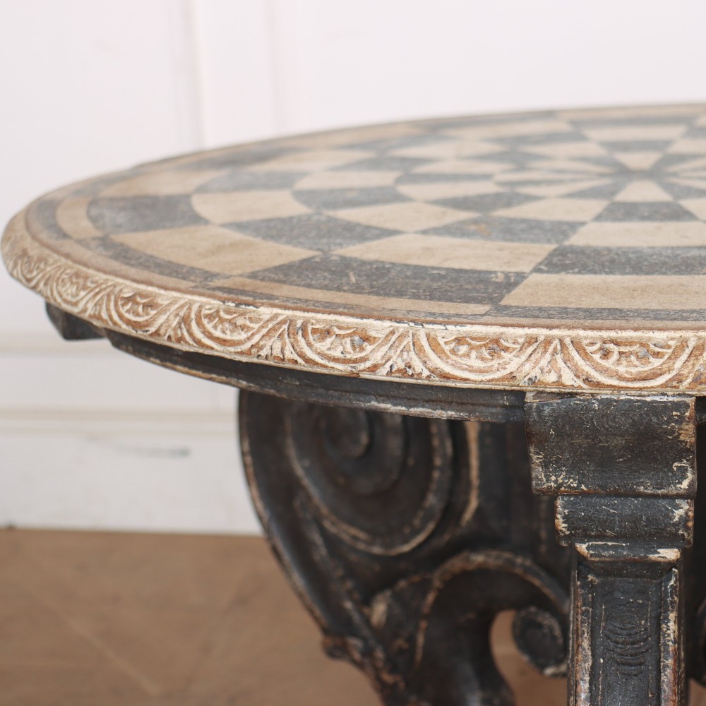 An antique round side table with a cream and grey circular checkerboard top supported by dark carved scroll legs with paw feet. View V