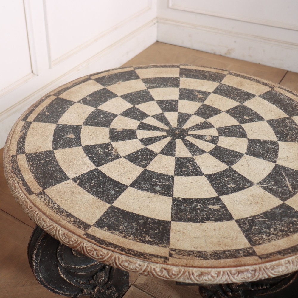 An antique round side table with a cream and grey circular checkerboard top supported by dark carved scroll legs with paw feet. View VIII