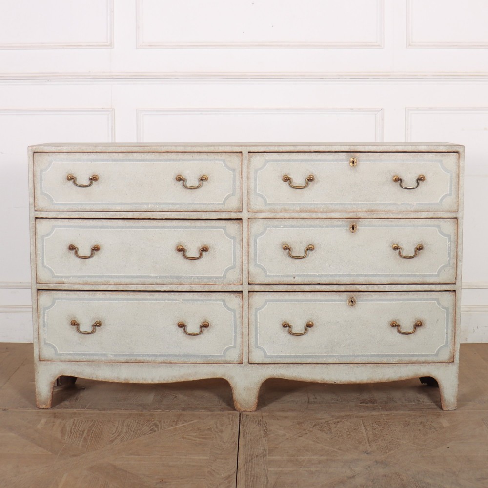 A wide pale grey painted chest featuring six drawers decorated with blue painted border outlines and brass drop handles.