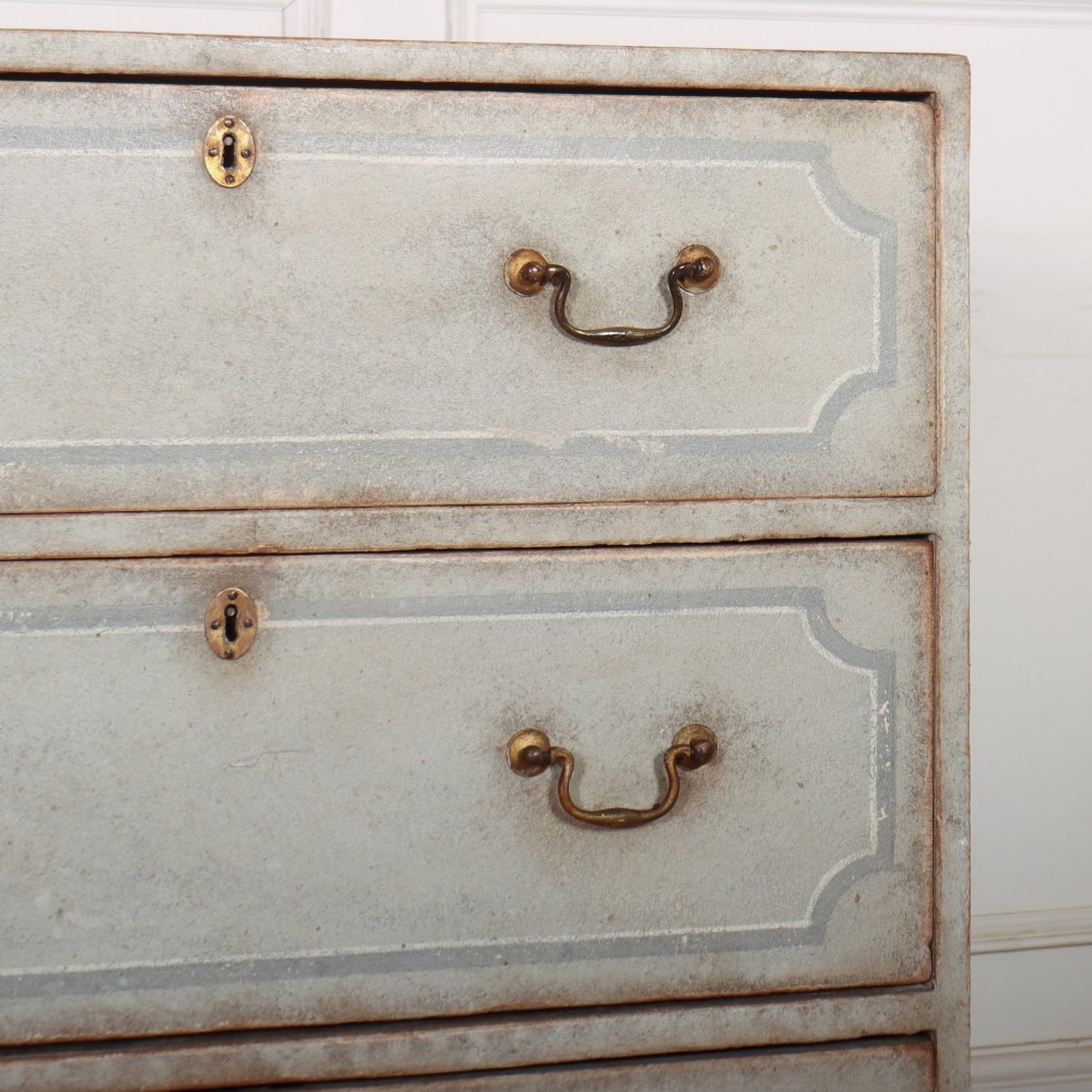 A wide pale grey painted chest featuring six drawers decorated with blue painted border outlines and brass drop handles. View VI