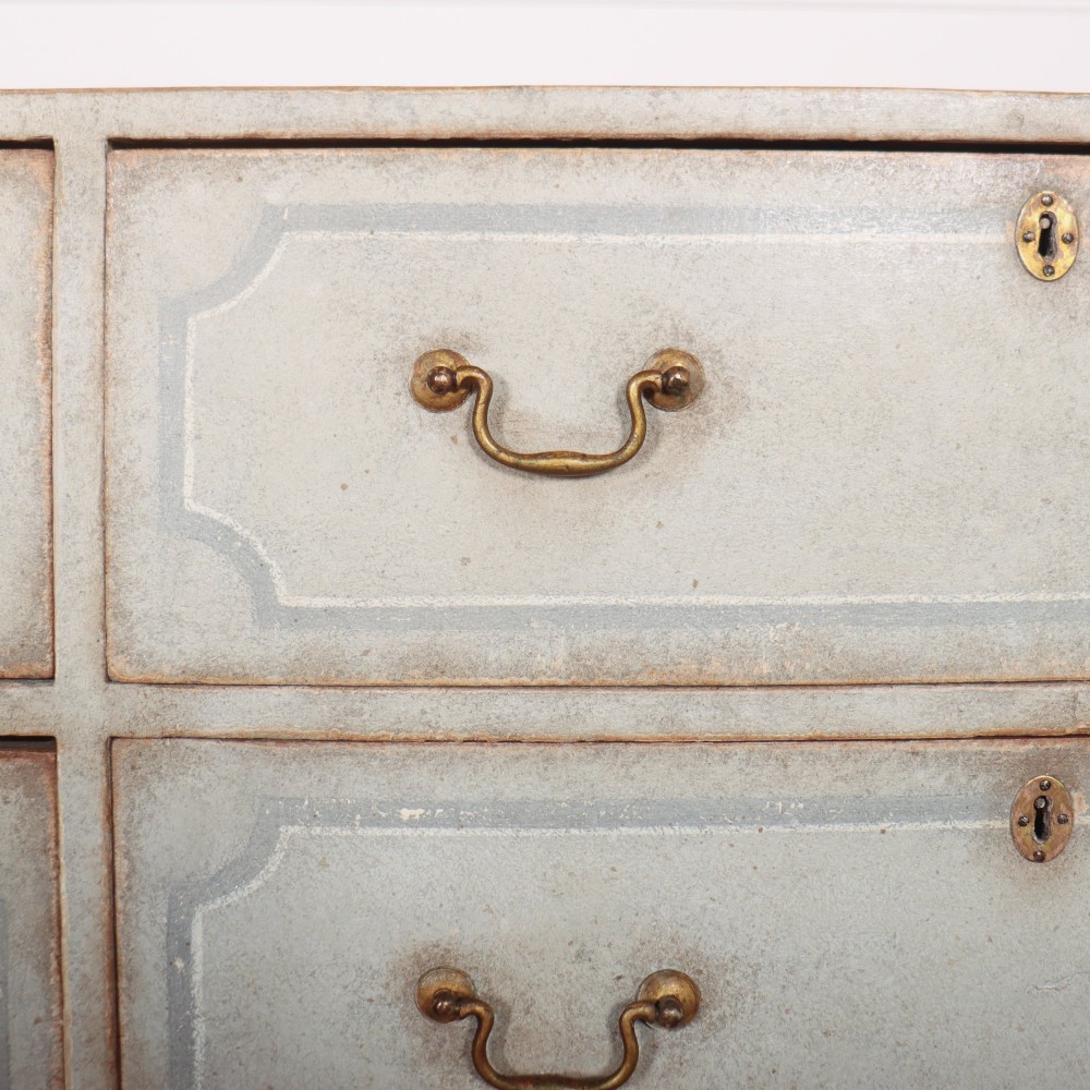 A wide pale grey painted chest featuring six drawers decorated with blue painted border outlines and brass drop handles. View VIII
