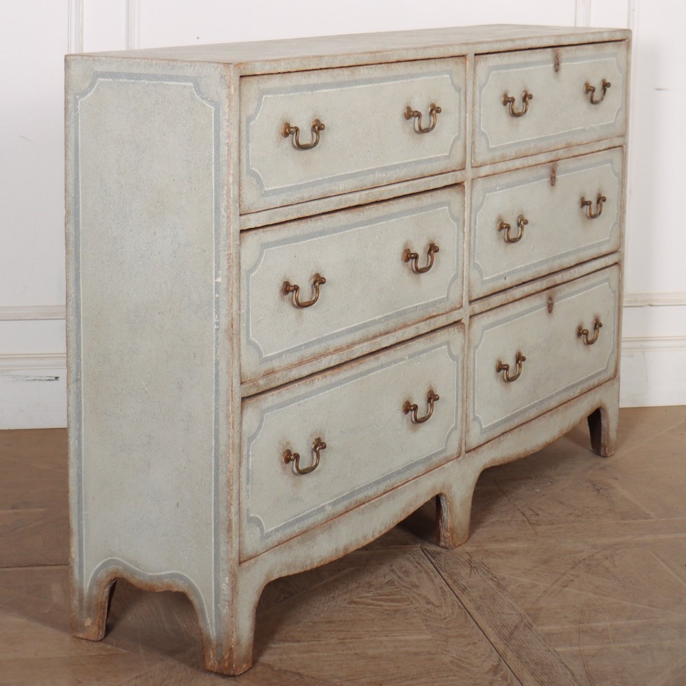 A wide pale grey painted chest featuring six drawers decorated with blue painted border outlines and brass drop handles. View IX