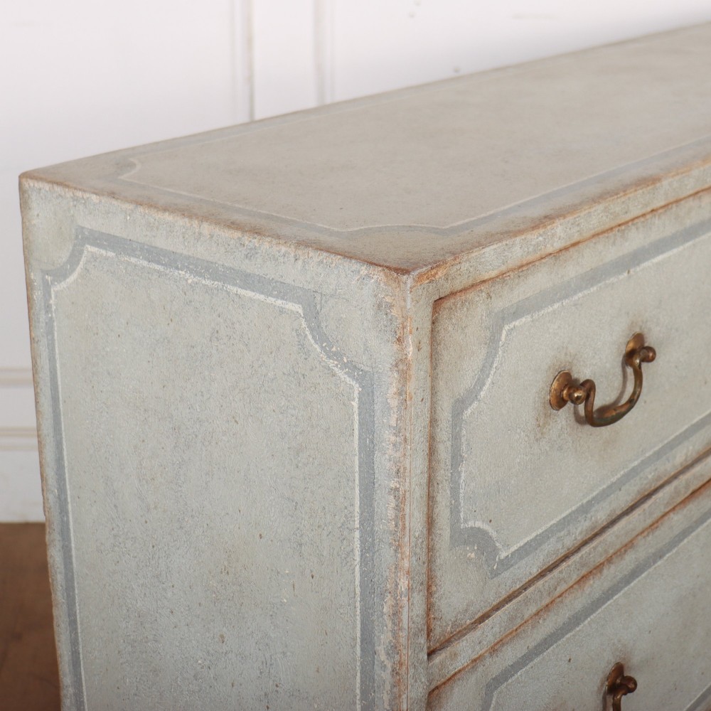 A wide pale grey painted chest featuring six drawers decorated with blue painted border outlines and brass drop handles. View X