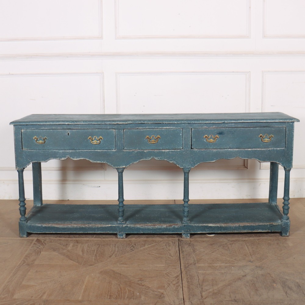 A long blue-painted wooden dresser base featuring three drawers with brass drop handles, a scalloped lower apron, turned front legs, and an open lower potboard shelf.
