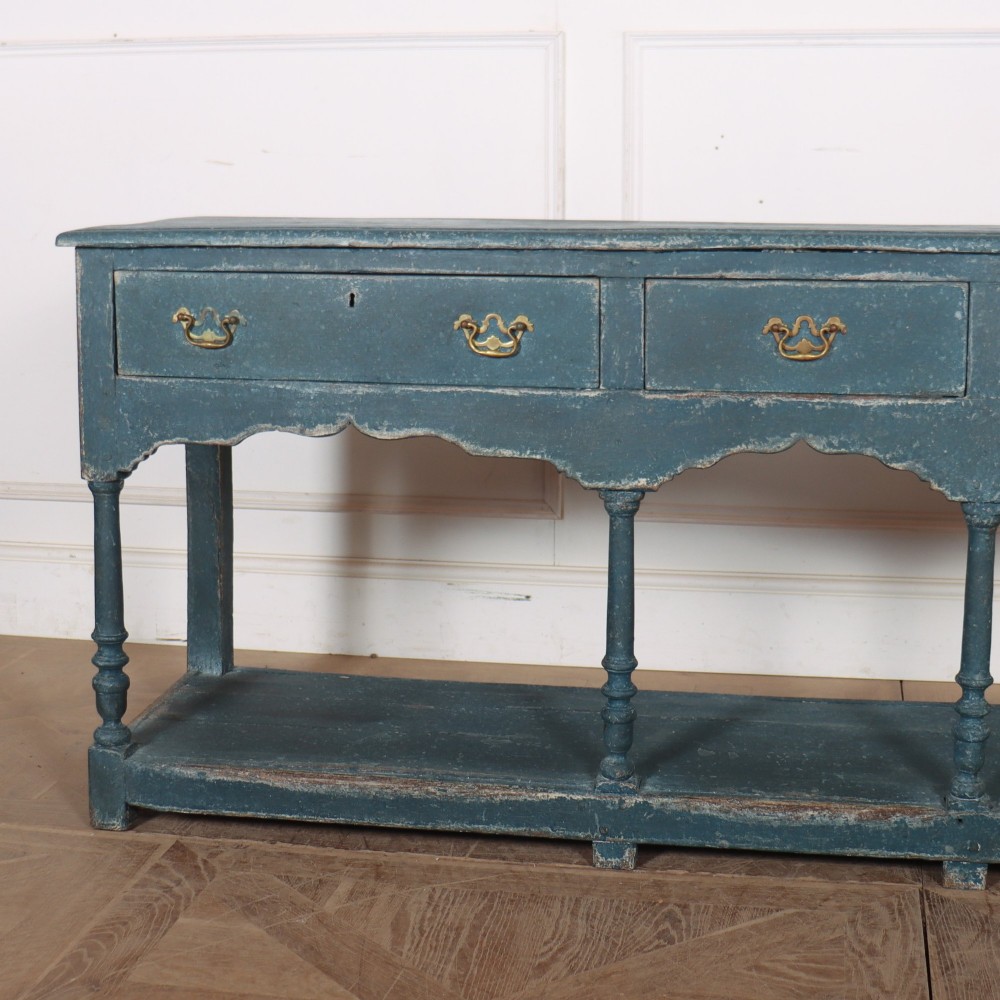 A long blue-painted wooden dresser base featuring three drawers with brass drop handles, a scalloped lower apron, turned front legs, and an open lower potboard shelf. View II