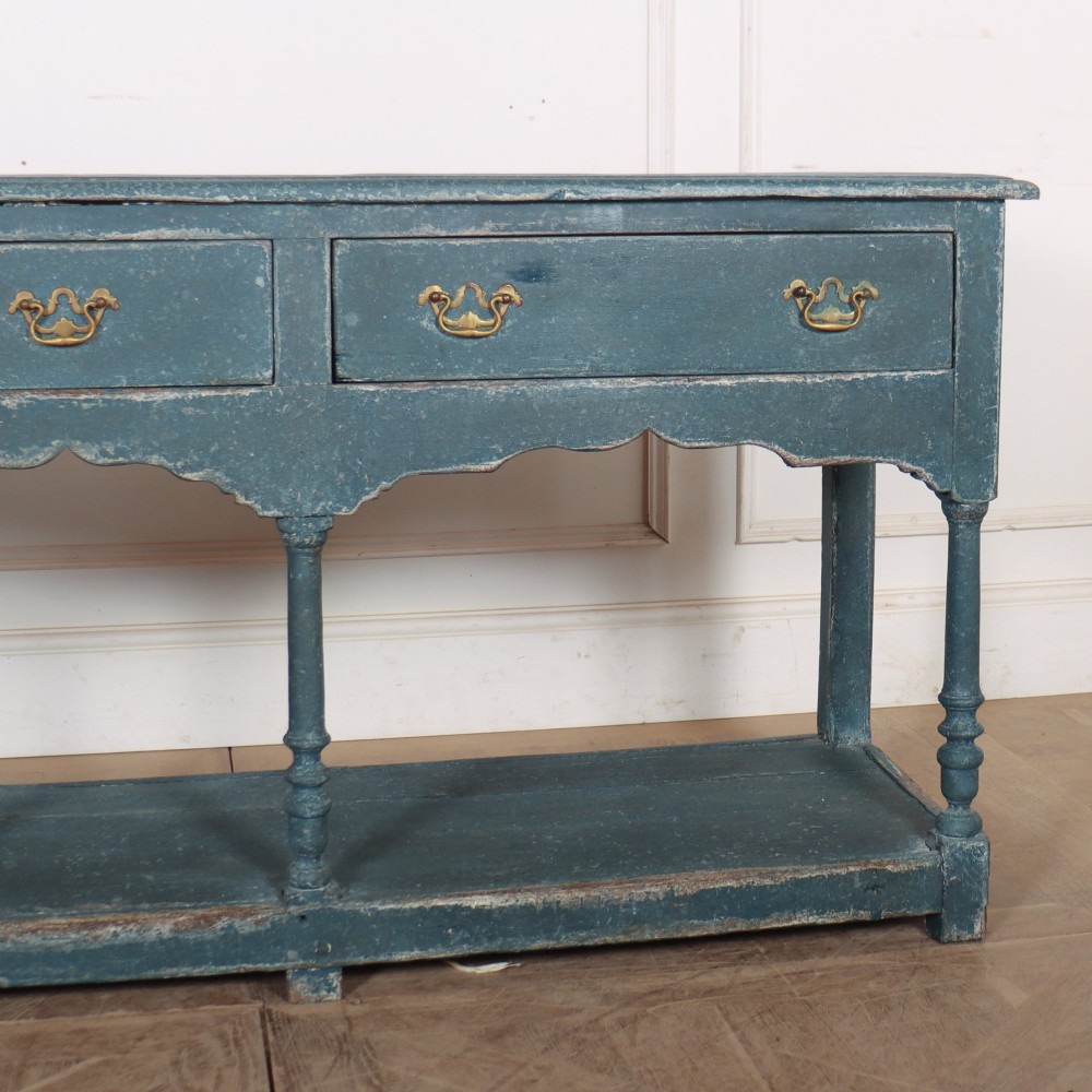 A long blue-painted wooden dresser base featuring three drawers with brass drop handles, a scalloped lower apron, turned front legs, and an open lower potboard shelf. View IV