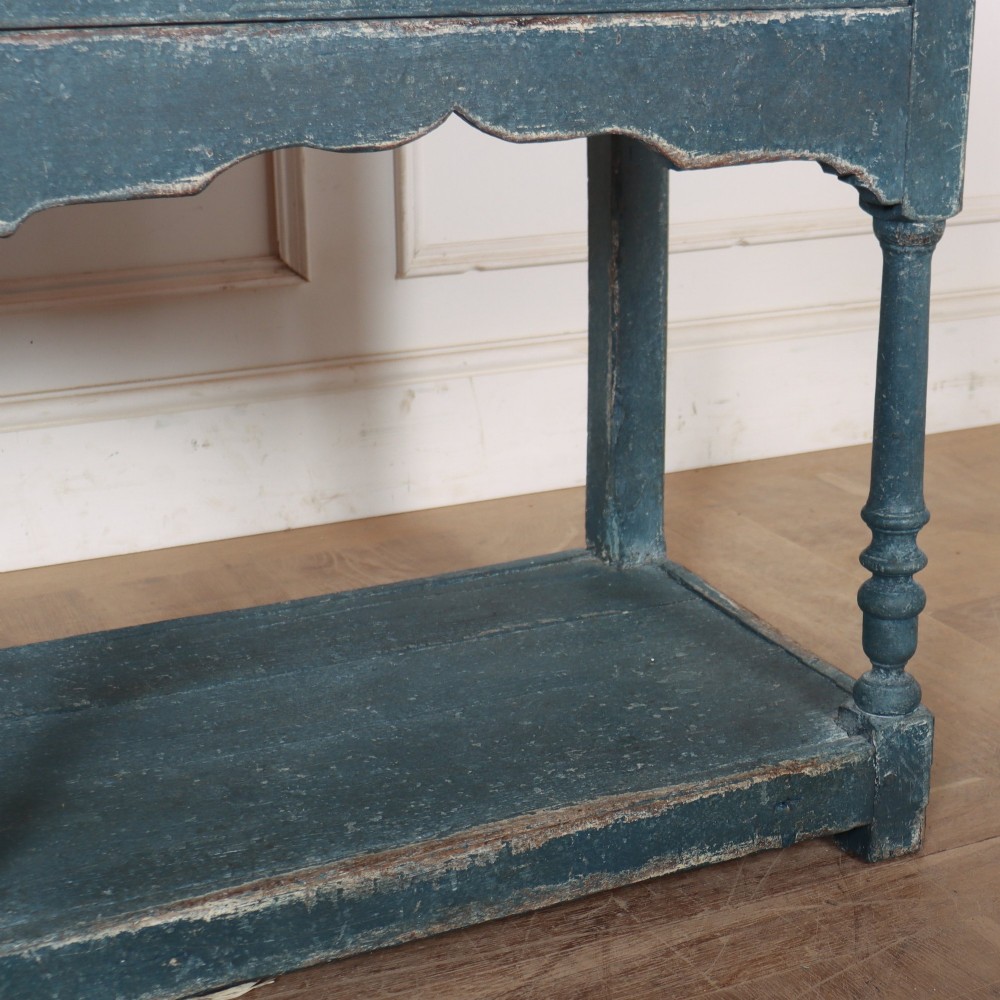 A long blue-painted wooden dresser base featuring three drawers with brass drop handles, a scalloped lower apron, turned front legs, and an open lower potboard shelf. View VI