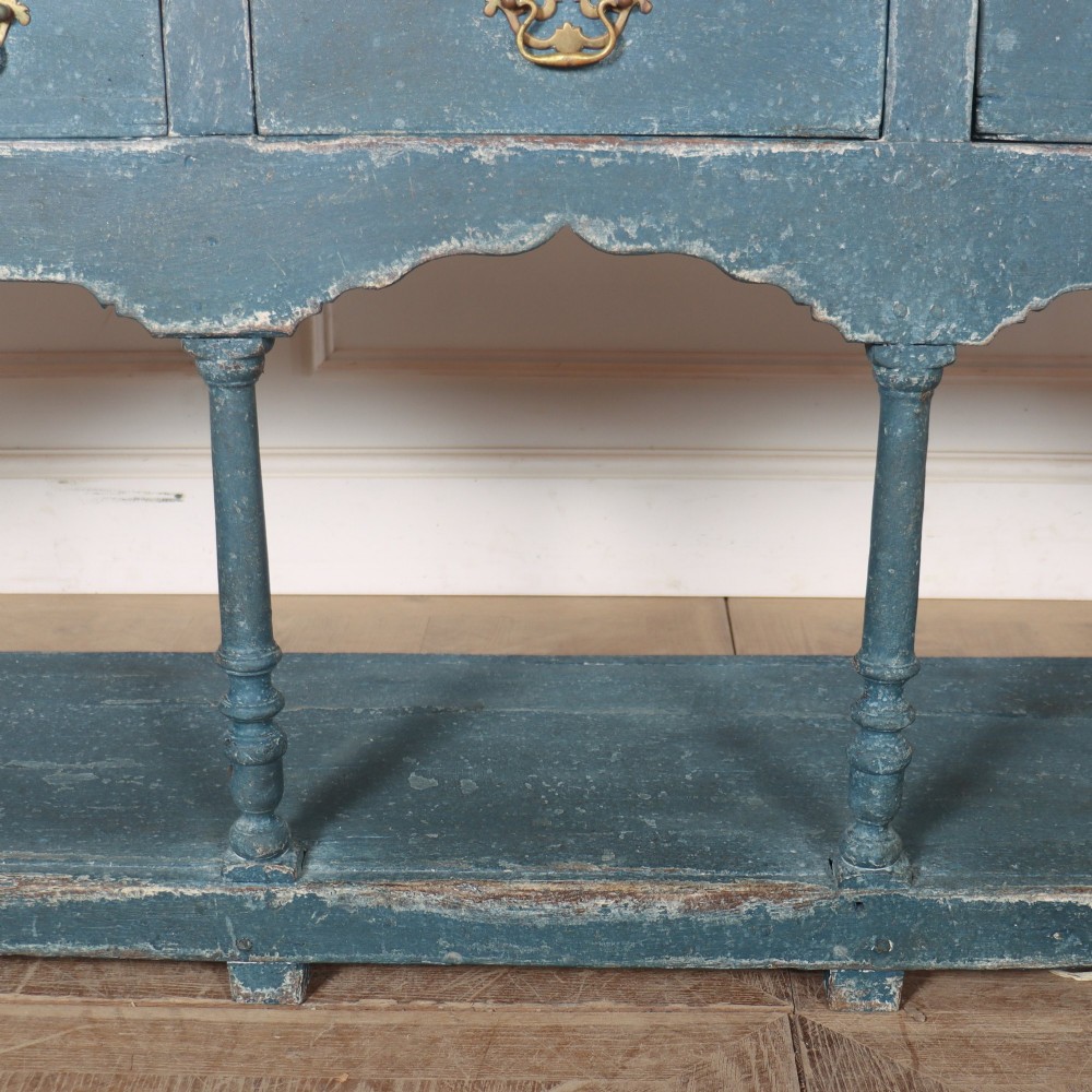 A long blue-painted wooden dresser base featuring three drawers with brass drop handles, a scalloped lower apron, turned front legs, and an open lower potboard shelf. View VII
