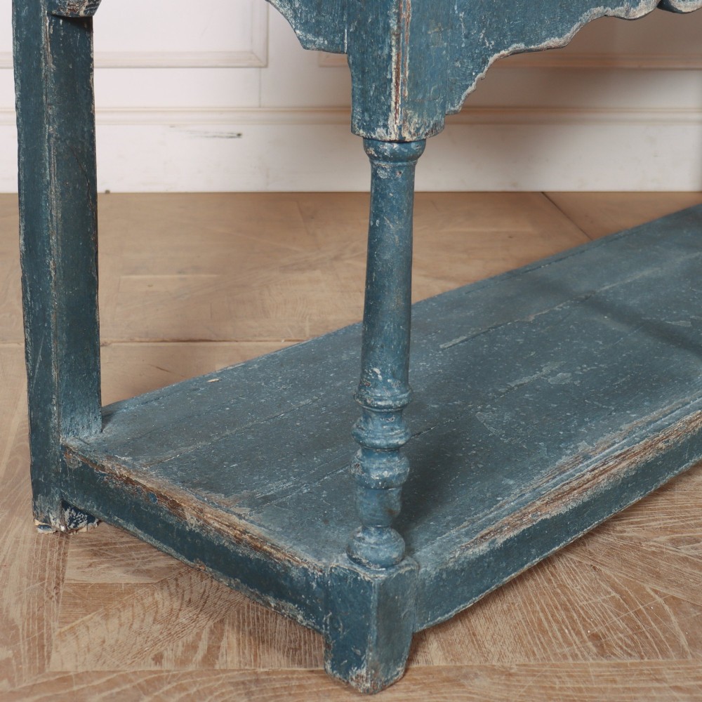 A long blue-painted wooden dresser base featuring three drawers with brass drop handles, a scalloped lower apron, turned front legs, and an open lower potboard shelf. View XI