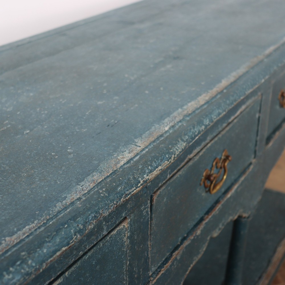 A long blue-painted wooden dresser base featuring three drawers with brass drop handles, a scalloped lower apron, turned front legs, and an open lower potboard shelf. View XIII