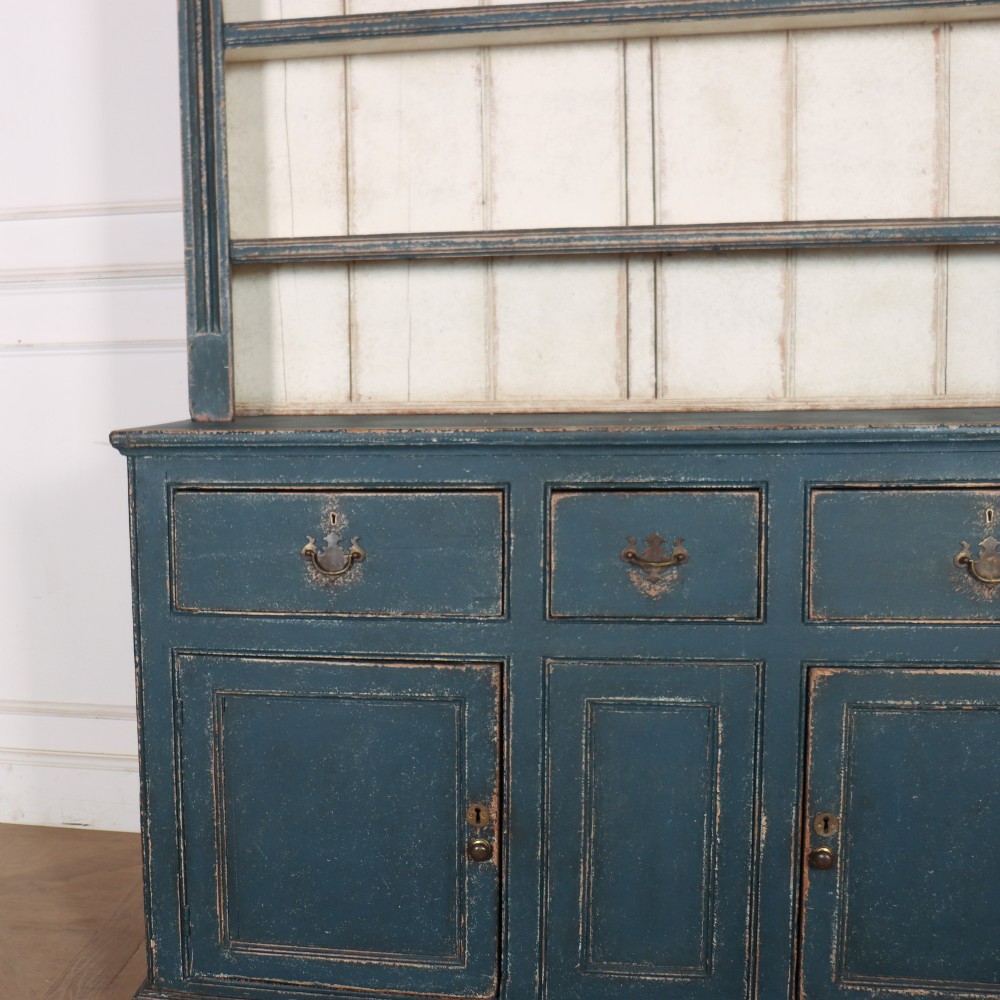 A large dark blue painted antique West Country dresser featuring an open plate rack with off-white backboards above three drawers and three panelled cupboard doors. View VI