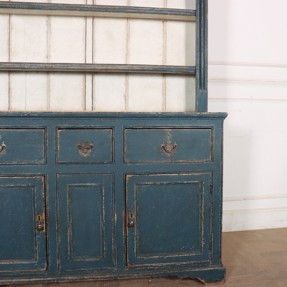 A large dark blue painted antique West Country dresser featuring an open plate rack with off-white backboards above three drawers and three panelled cupboard doors. View VII