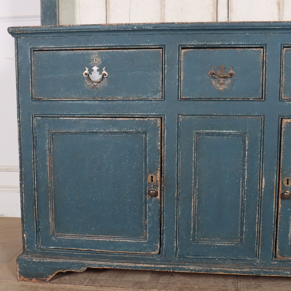 A large dark blue painted antique West Country dresser featuring an open plate rack with off-white backboards above three drawers and three panelled cupboard doors. View IX