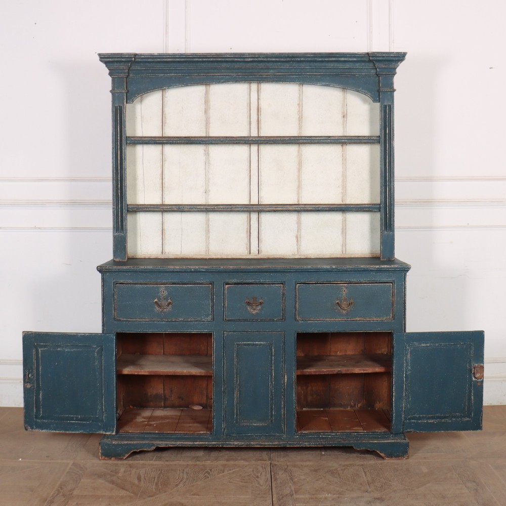 A large dark blue painted antique West Country dresser featuring an open plate rack with off-white backboards above three drawers and three panelled cupboard doors. View X