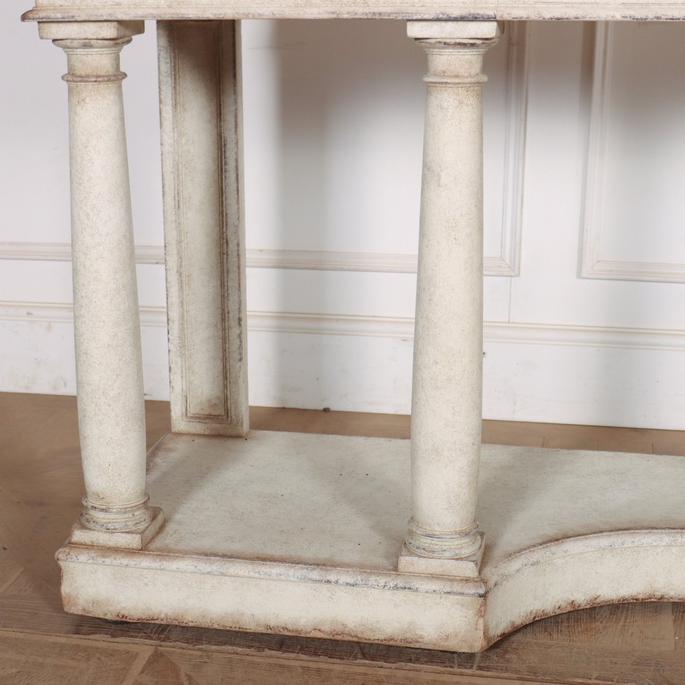 An antique off-white painted console table featuring a light marble top, three drawers with brass handles, four column supports, and a curved lower shelf. View III