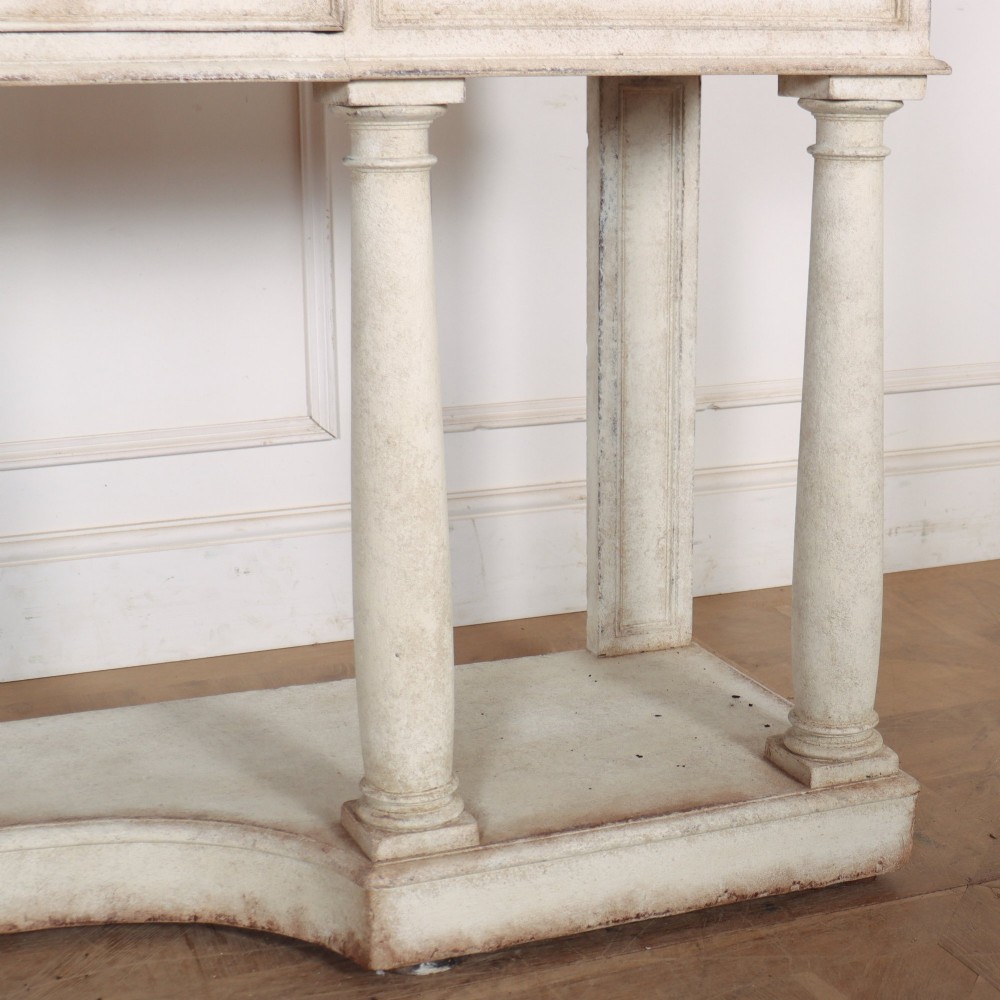 An antique off-white painted console table featuring a light marble top, three drawers with brass handles, four column supports, and a curved lower shelf. View V