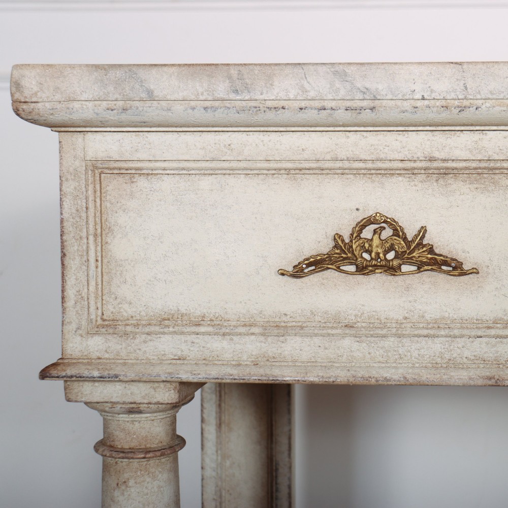 An antique off-white painted console table featuring a light marble top, three drawers with brass handles, four column supports, and a curved lower shelf. View VI