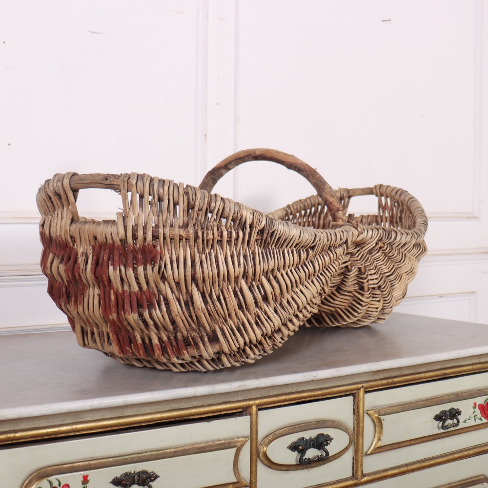 A double-compartment woven wicker grape harvesting basket featuring a central bentwood handle and red painted markings along the woven side.