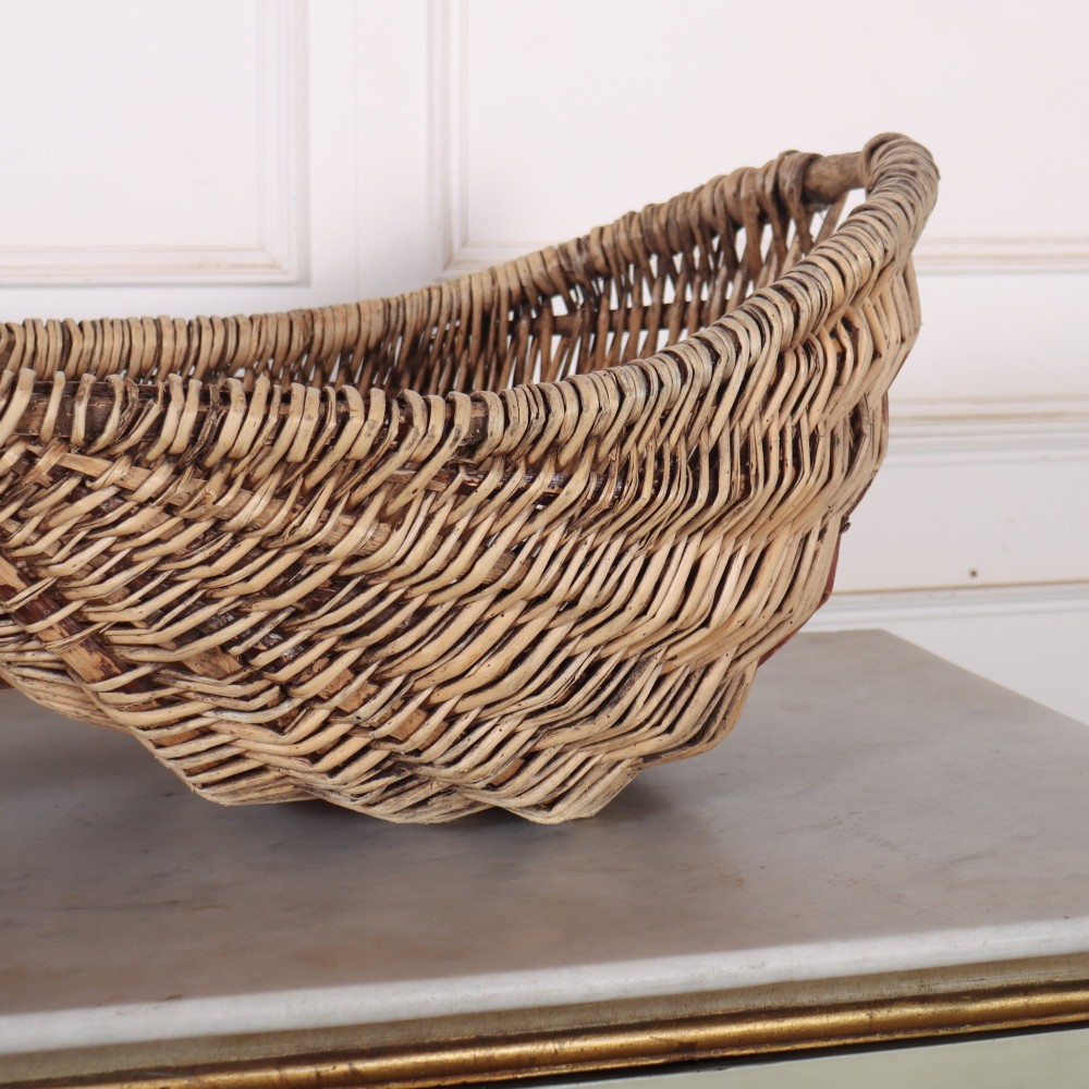 A double-compartment woven wicker grape harvesting basket featuring a central bentwood handle and red painted markings along the woven side. View III