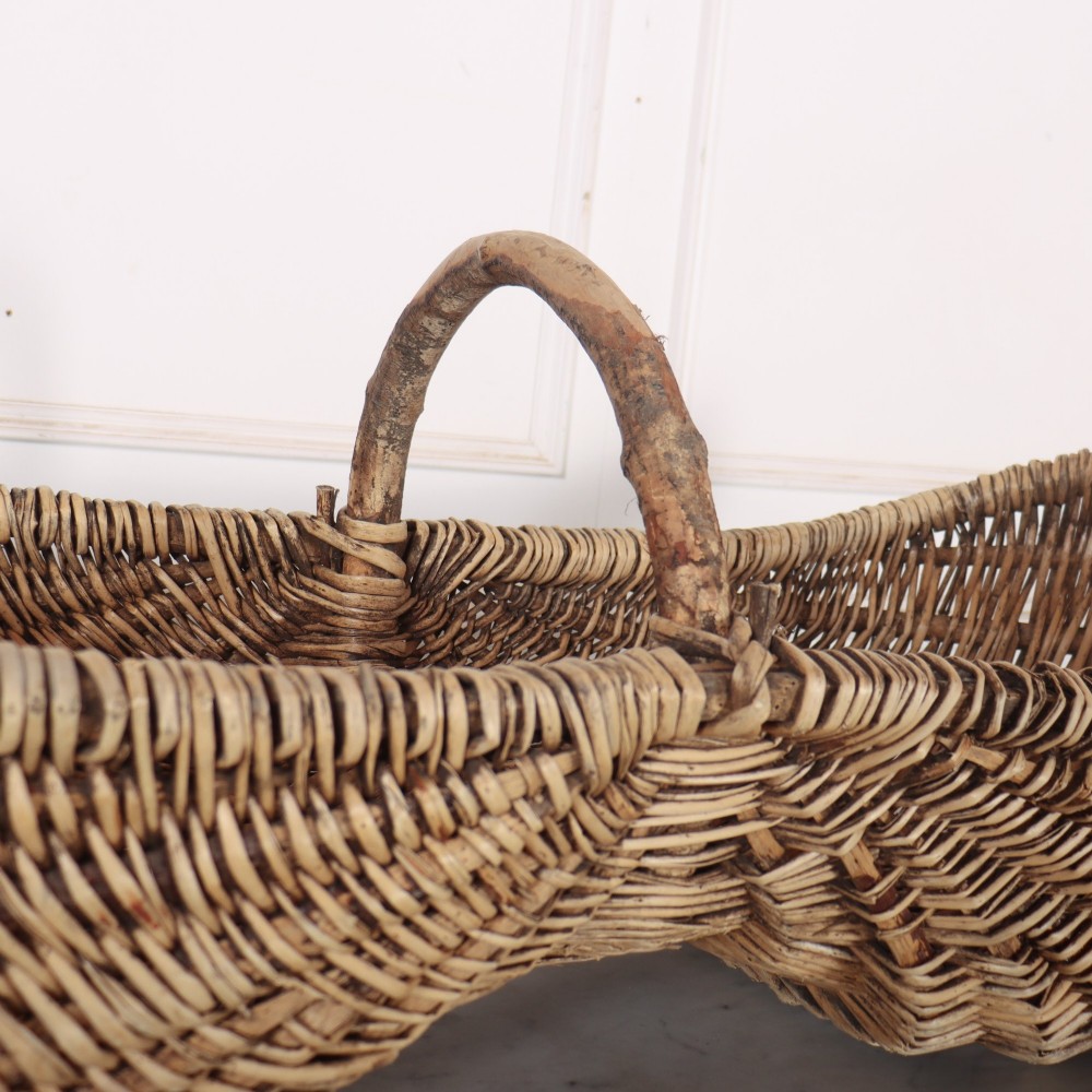 A double-compartment woven wicker grape harvesting basket featuring a central bentwood handle and red painted markings along the woven side. View V