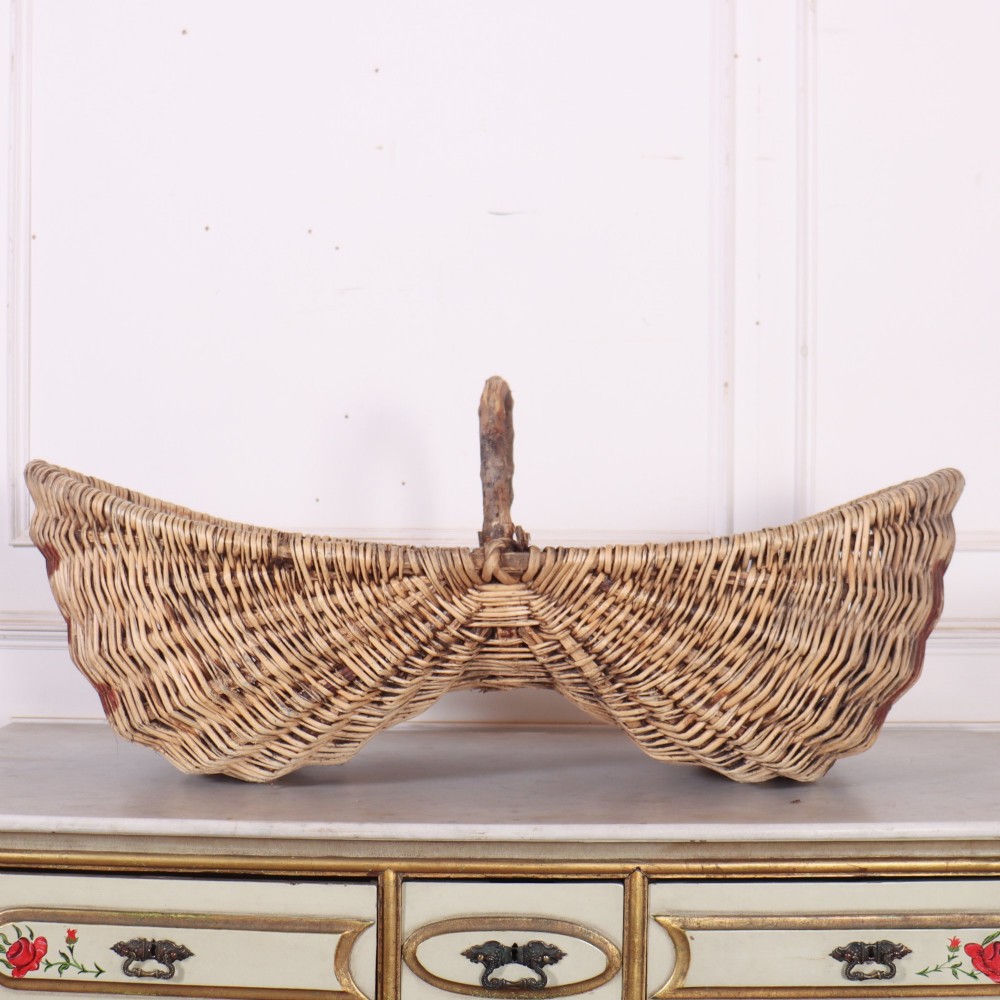 A large woven wicker twin harvest basket featuring a bentwood central handle and faded red painted marks on the natural exterior. View II
