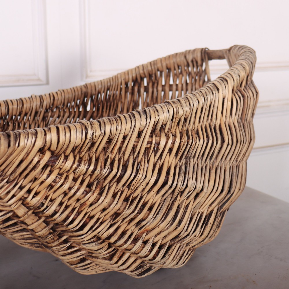 A large woven wicker twin harvest basket featuring a bentwood central handle and faded red painted marks on the natural exterior. View III