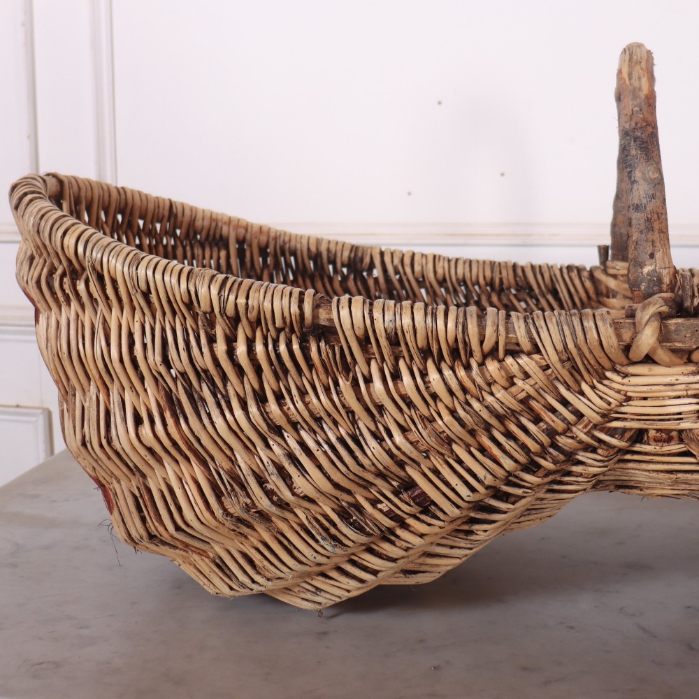 A large woven wicker twin harvest basket featuring a bentwood central handle and faded red painted marks on the natural exterior. View IV